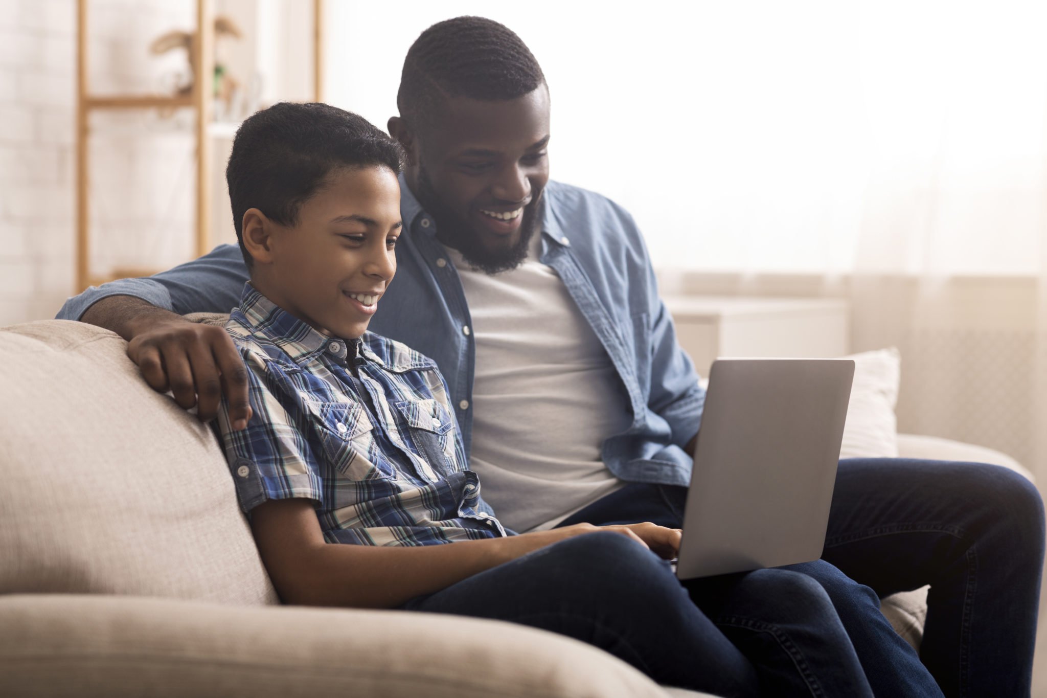 Cheerful afro boy and his father using laptop computer at home