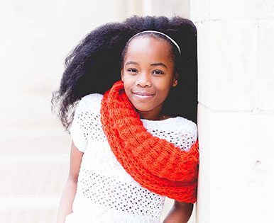 A girl with a red scarf smiling back to the camera.